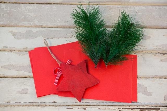 Red envelopes and fir branches with a star decoration on a rustic wooden plank. Perfect for holiday greeting cards, festive invitations, Christmas crafts, and seasonal decorations.