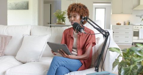 Woman recording podcast from bright living room using tablet and condenser microphone