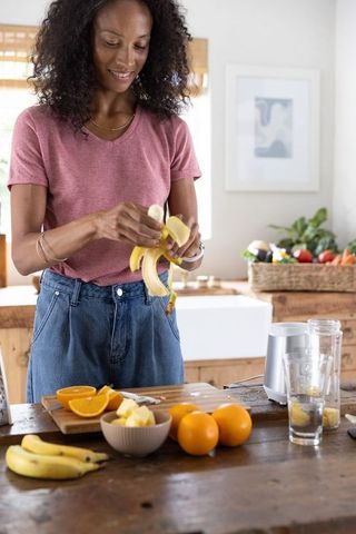 African american woman preparing banana orange smoothie on rustic wooden kitchen island