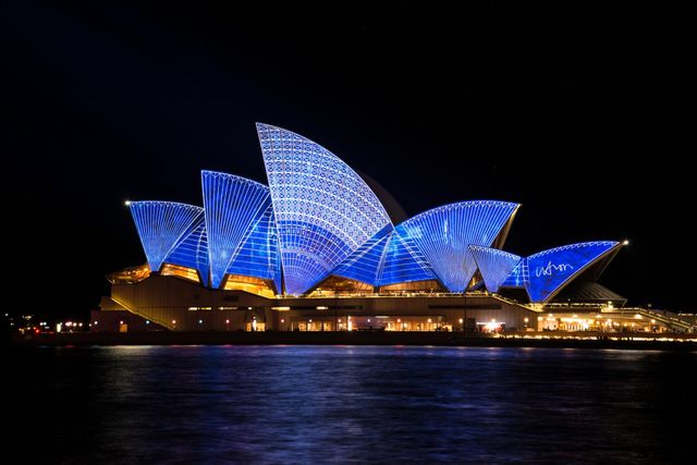 Sydney Opera House illuminated in vibrant blue lights at night. Ideal for use in travel brochures, tourism websites, architecture portfolios, cultural publications, and event promotions.