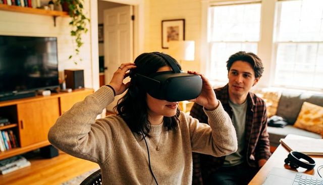 Woman testing tethered vr headset in cozy midcentury living room while partner watches