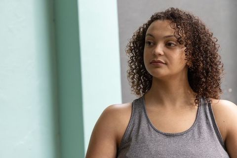 African-american woman standing by teal column in urban athletic portrait with curly hair