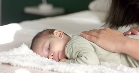 Mother Soothing Sleeping Infant on Soft Bed