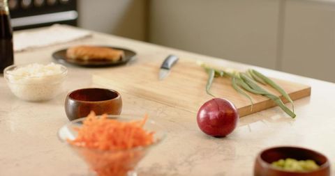 Red onion sitting on light countertop with cutting board, knife and fresh scallions