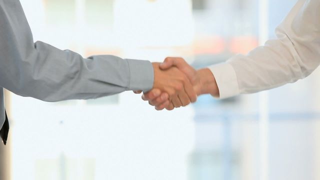 Two businessmen are seen shaking hands in an office location, reflecting professional relationships and successful negotiations. This image symbolizes agreement, partnership, and teamwork, making it ideal for use in business presentations, websites, and marketing materials that illustrate corporate collaboration and trust.