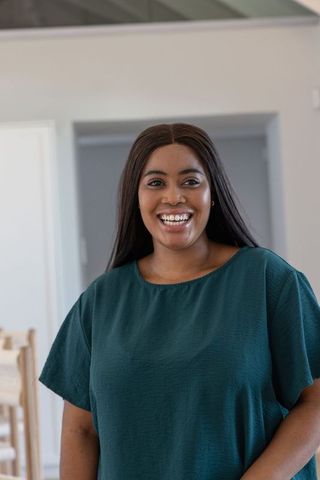 African american woman smiling and standing at home in teal blouse
