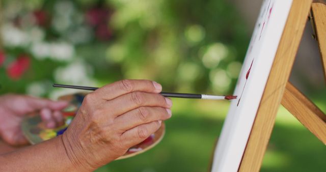 Image of hands of biracial senior woman painting in garden. active retirement lifestyle, hobby and spending time outdoors.