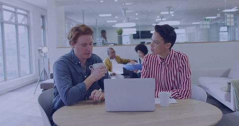 Business-casual colleagues collaborating over laptop and coffee in modern office lounge