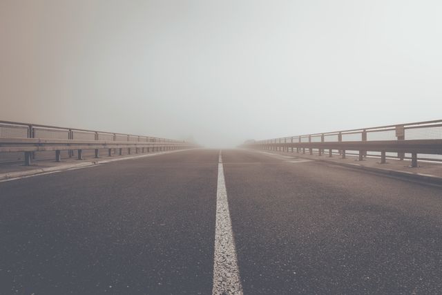 This photo shows an empty foggy road stretching towards the horizon with very low visibility. The mist and overcast weather give the scene an eerie and desolate mood. It may be used to convey concepts like journey, uncertainty, isolation, or transportation in various projects including blog posts, websites, and advertisements.