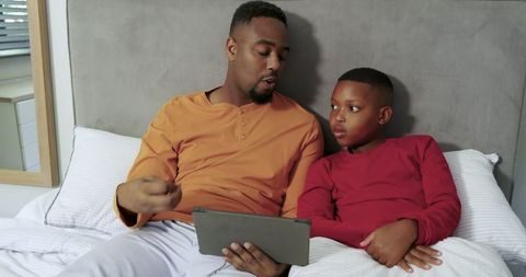 Father and Son Relaxing on Bed Sharing Tablet Time