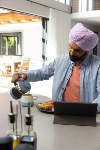 Man with Turban Having Breakfast Coffee While Using Tablet in Modern Kitchen