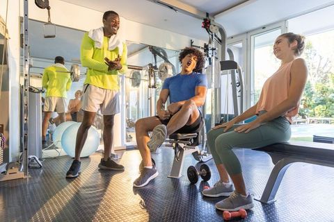 Friends laughing and stretching in bright home gym with energy and camaraderie