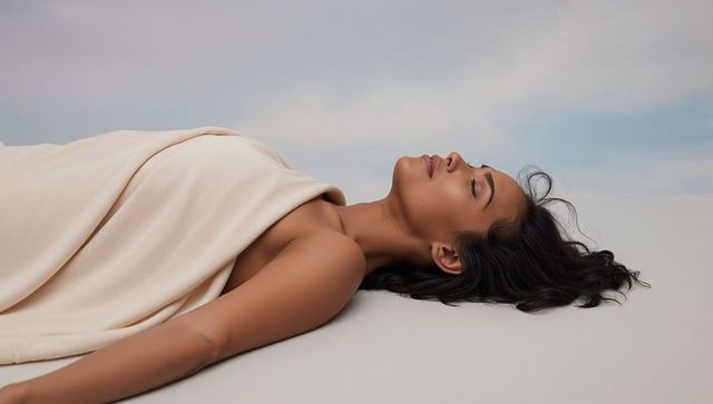 Serene reclining woman supine on pale backdrop wrapped in soft beige drape