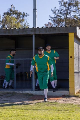 Baseball teammates stepping out of dugout in green uniforms celebrating team moment