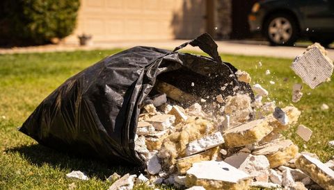 Torn black garbage bag spilling drywall and yellow insulation across suburban lawn