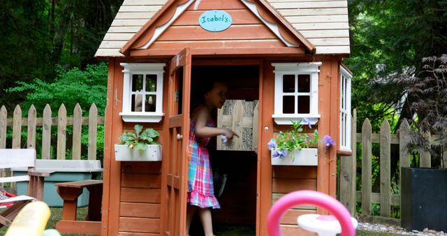 Young child enjoying playtime in a wooden playhouse in a garden. Perfect for articles on outdoor activities, summer fun, family play, childhood memories, and backyard setup.