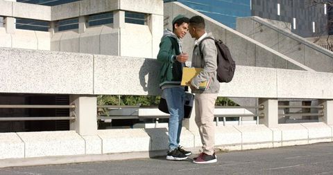 Two african american male students conversing on urban pedestrian bridge with backpacks