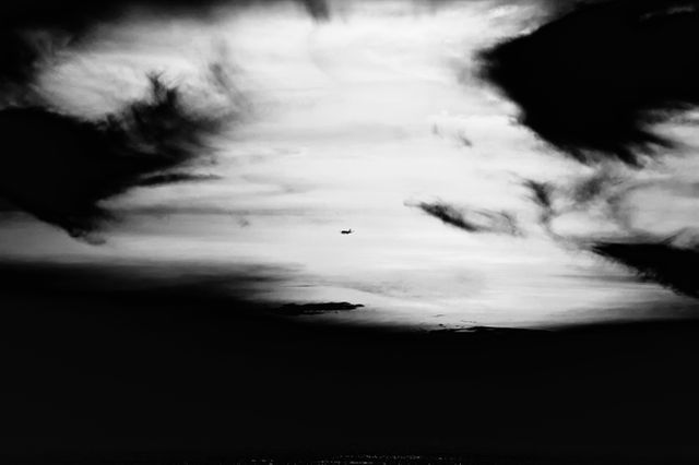 Black and white scene of an airplane flying through a dramatic evening sky with striking cloud formations. Ideal for articles, websites, or advertisements related to travel, aviation, tranquility, or mood-setting visuals. Could also be used in artistic designs emphasizing contemplation, freedom, or minimalism.