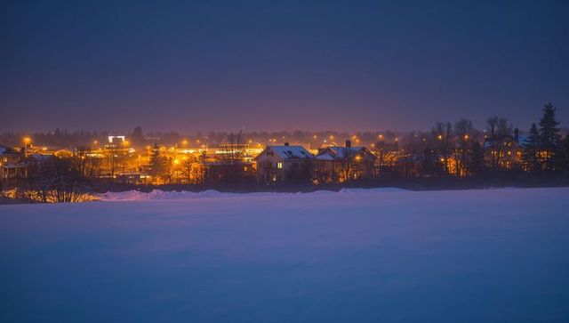 Suburban neighborhood glowing over snowfield at twilight with warm streetlight glow