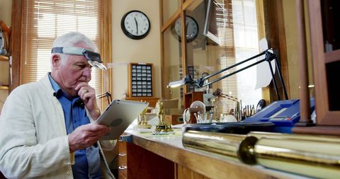 Elderly horologist using digital tablet in classic workshop