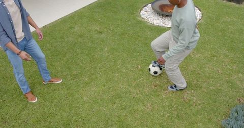 Overhead view of two men playing casual soccer on backyard lawn with patio and garden