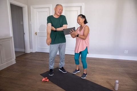 Chinese senior couple exercising at home using tablet for guided workout and stretching