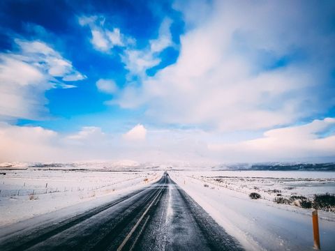 Endless Winter Highway Stretching to Snowy Horizon under Dramatic Blue Sky and Clouds