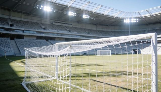 Sunlit soccer goal and net in modern stadium with exposed roof trusses and field shadows