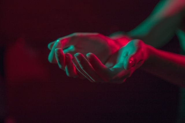 Moody hands lit with red and green lighting creating an artistic silhouette effect. Useful for artistic projects, expressive visual content, dramatic scenes, marketing materials focusing on emotions or expressive storytelling.