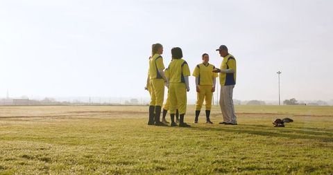 Coach Motivating Diverse Softball Team in Yellow Jerseys on Field