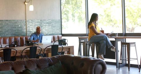 Woman working on laptop at sunlit cafe counter with relaxed coworking atmosphere