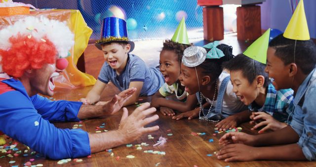 A clown entertains a diverse group of children at a birthday party, with copy space. Laughter and joy are evident as the kids, wearing party hats, engage with the performer's antics.