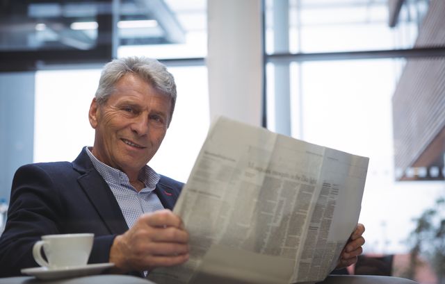Senior businessman reading newspaper while enjoying coffee in a modern office. Ideal for use in business, corporate, and professional contexts, as well as for illustrating concepts of relaxation, morning routines, and staying informed in the workplace.