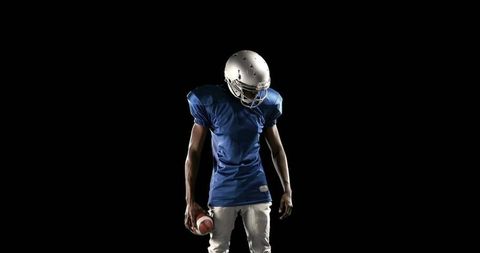 Standing American Football Player Holding Ball in Dramatic Spotlight Wearing Blue Jersey