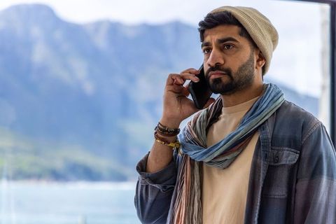Thoughtful traveler calling on smartphone while standing by mountain lake window