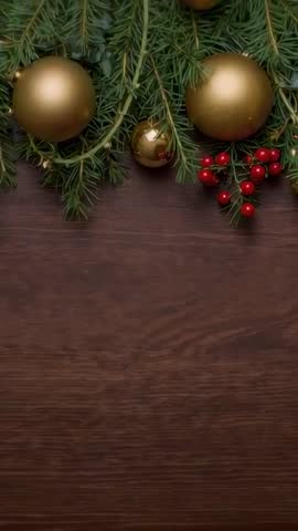 Fir garland settling on dark wood table with gold baubles and red berries vertical video