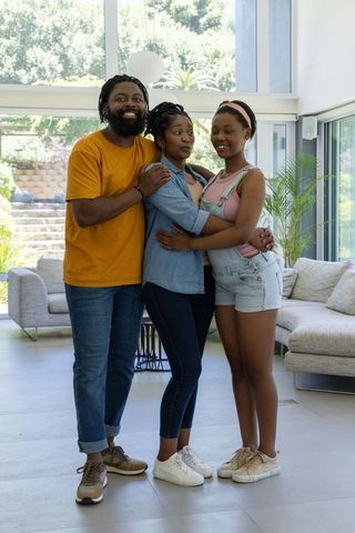 African family hugging teenage daughter in sunlit modern living room with large windows