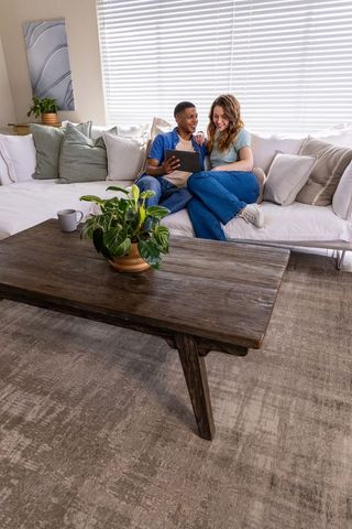 Diverse couple relaxing on white sofa sharing tablet in cozy neutral living room