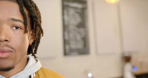 African american man with dreadlocks wearing mustard jacket and hoodie in cafe with copy space