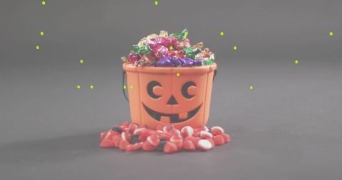 Halloween pumpkin bucket overflowing with colorful wrapped candies and red candy mix