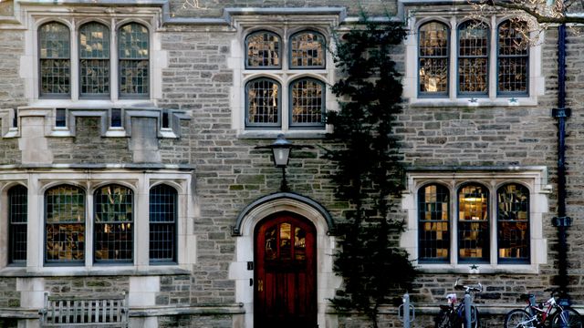 A well-preserved historic stone building featuring distinctive Gothic architectural elements and climbing ivy on the wall. Perfect for use in educational materials, travel brochures, and historical documentaries or articles showcasing architectural heritage and classic university settings.