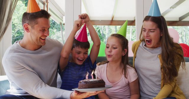 Portrait of caucasian girl in party hat blowing candles on birthday cake while family smiling and waving looking at the camera at home. social distancing during coronavirus quarantine lockdown.