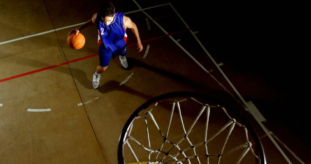 Basketball player dribbling on court during night game, viewed from above. Ideal for articles, ads, and content related to sports, athleticism, and basketball games. Use in sports blogs, training materials, or websites focusing on team sports and athletic events.