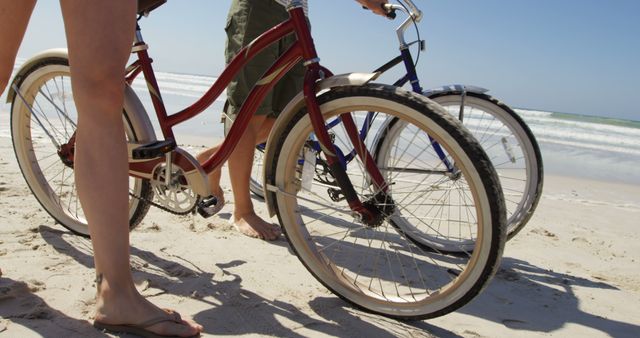 This image captures a close-up view of two individuals biking along a sandy beach with the ocean waves in the background. Their focus is on travel, but the vibrant hues of the bicycles paired with the natural sand and sea setting create a mood of leisure and relaxation. This versatile image is perfect for advertisements about beach vacations, outdoor activities, healthy lifestyles, and travel destinations.
