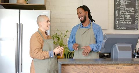 Diverse baristas chatting and smiling behind cafe counter pointing at register