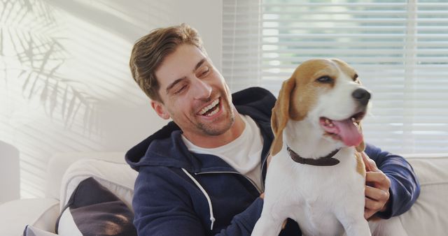 A young Caucasian man enjoys a playful moment with his pet beagle, both appearing cheerful and content. Their bond exemplifies the joy and companionship pets bring to their owners' lives.