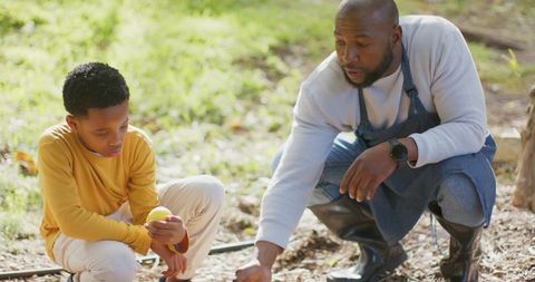 African american father teaching son gardening while examining small yellow seed ball outdoors