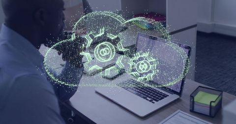 Holographic cloud gears hovering over laptop for team collaboration in modern office