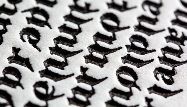 Macro close-up of embossed blackletter calligraphy on textured paper casting deep shadows