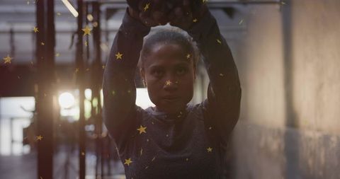 Determined woman training with arms raised under dramatic backlight and gold-star reflections